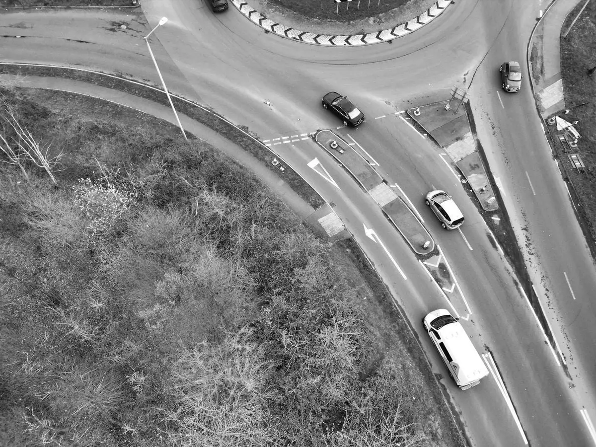 Aerial shot of a roundabout with cars, showing traffic flow and road design, in black and white.