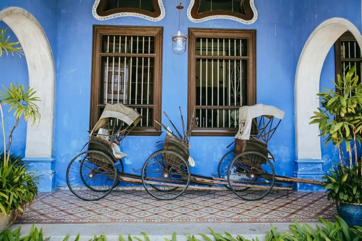 Two vintage rickshaws rest against a vibrant blue wall in George Town, Malaysia.