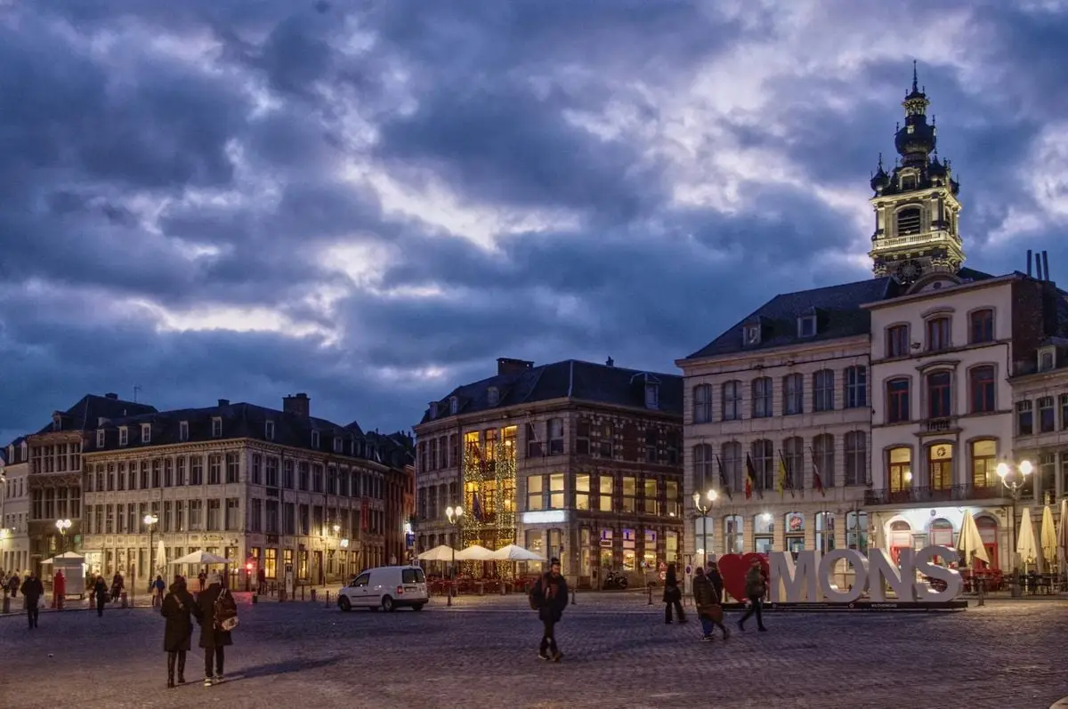 Scenic view of Mons city center at twilight with historic buildings and illuminated signs.