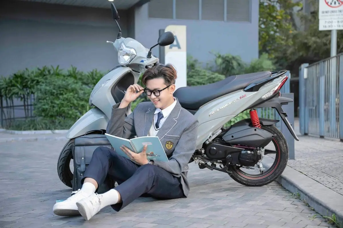 Vietnamese student reading by a scooter outdoors, showcasing urban lifestyle.