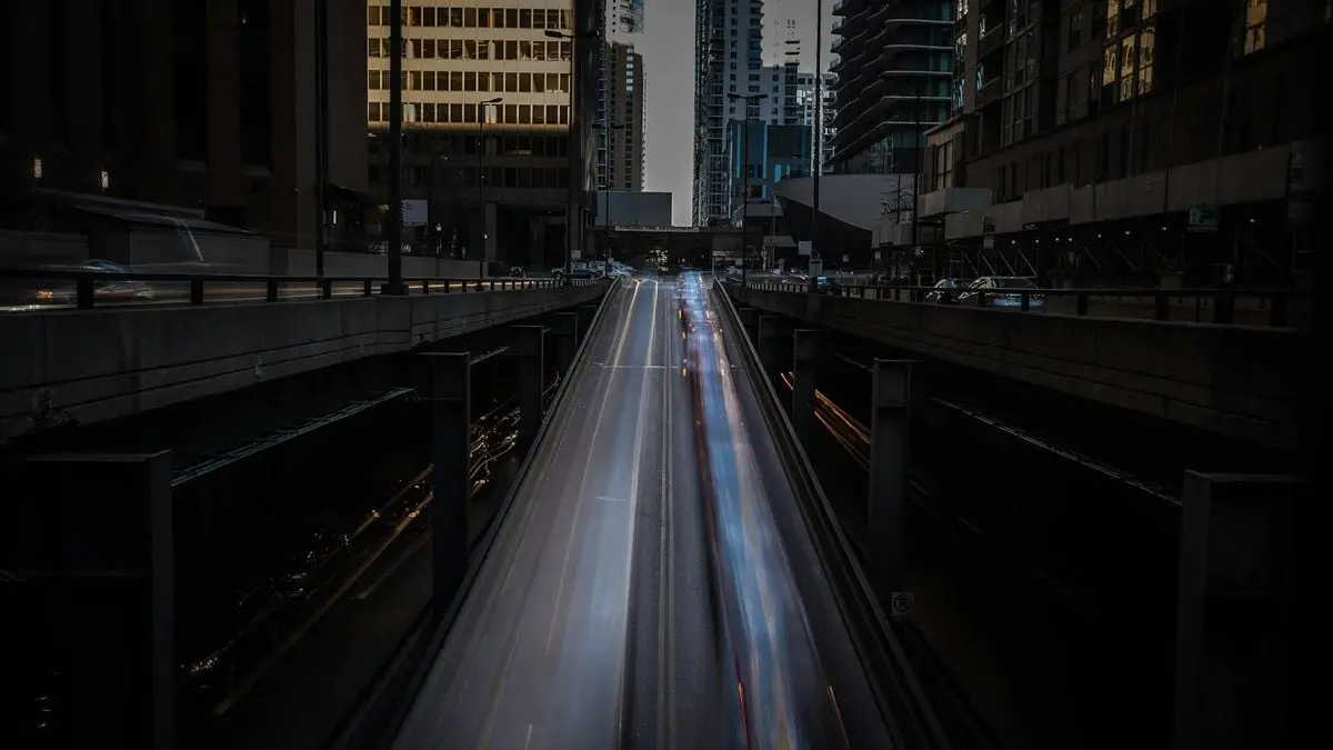 Long exposure of city highway at night featuring light trails and modern buildings.