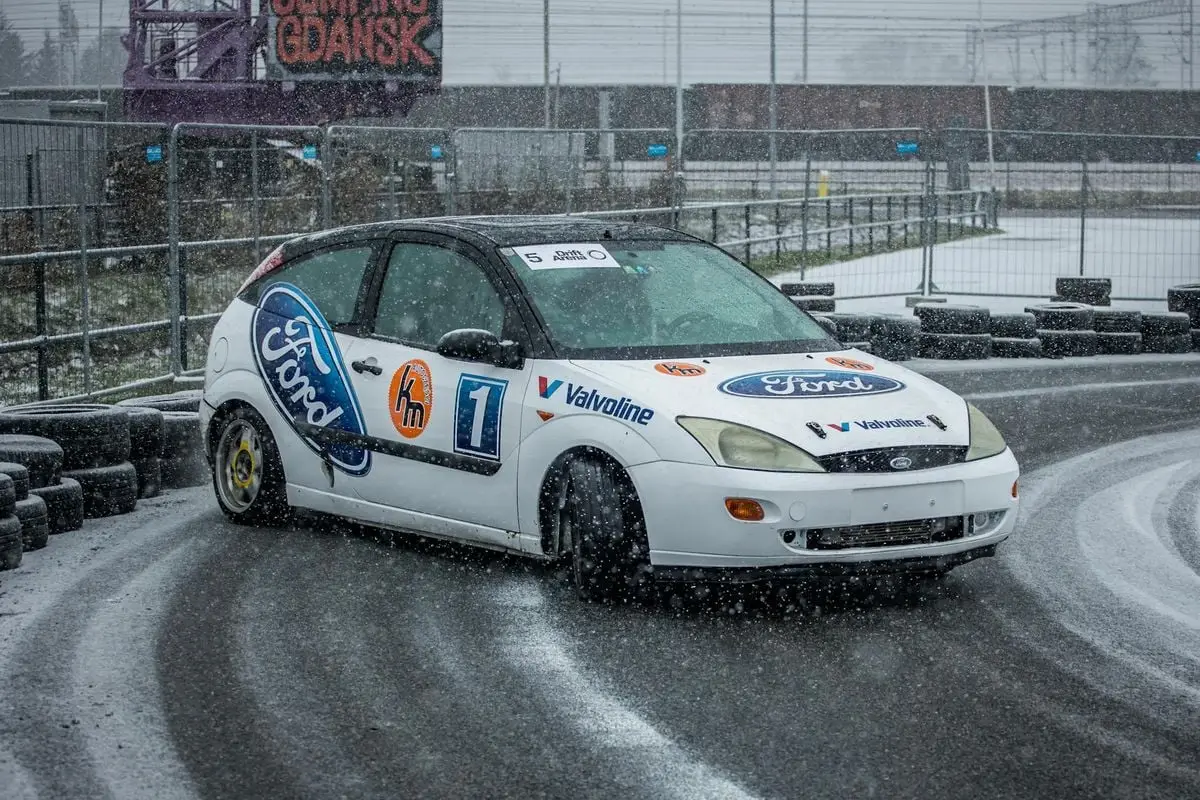 A Ford car drifts on a snowy racetrack in Gdańsk, showcasing motorsport excitement.