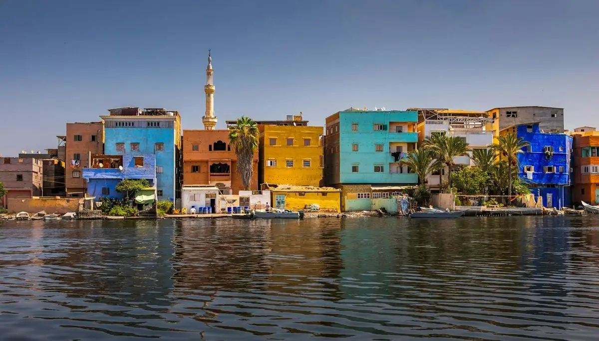 Bright colorful buildings along a riverside with a mosque in the background, capturing a lively townscape.