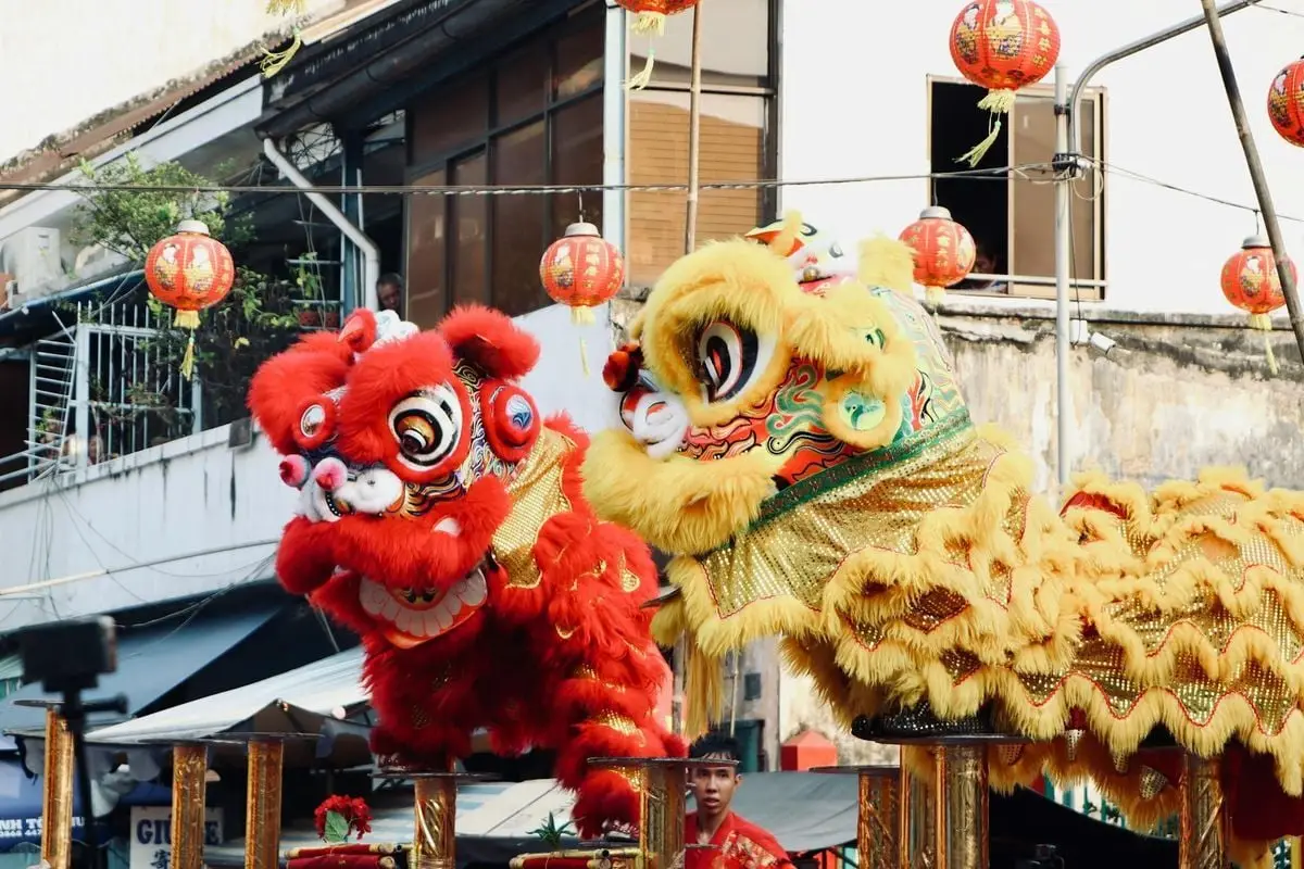 Colorful lion dance performance with red and yellow costumes at a cultural festival, featuring traditional lanterns.