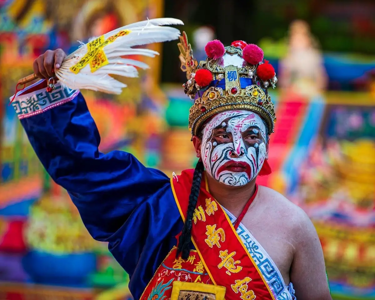 Vibrant portrayal of a performer in traditional clothing and creative makeup at a Taiwanese festival.
