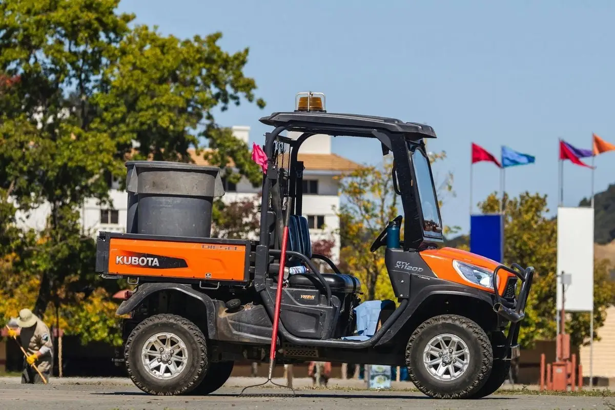 Orange Kubota RTV on display outdoors with flags in the background.