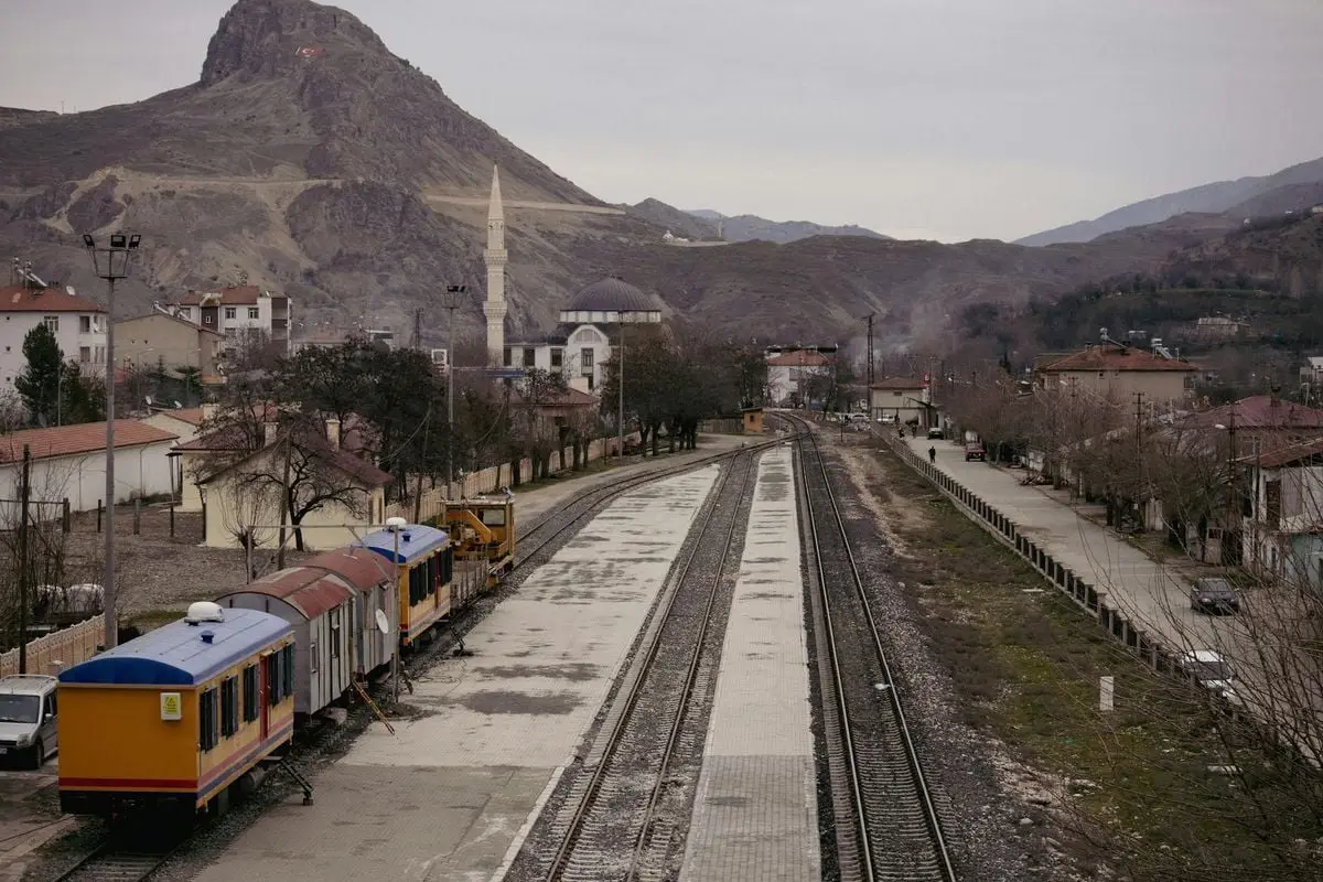 A tranquil railway station in Palu, Elazığ with a mosque, mountain, and trains.