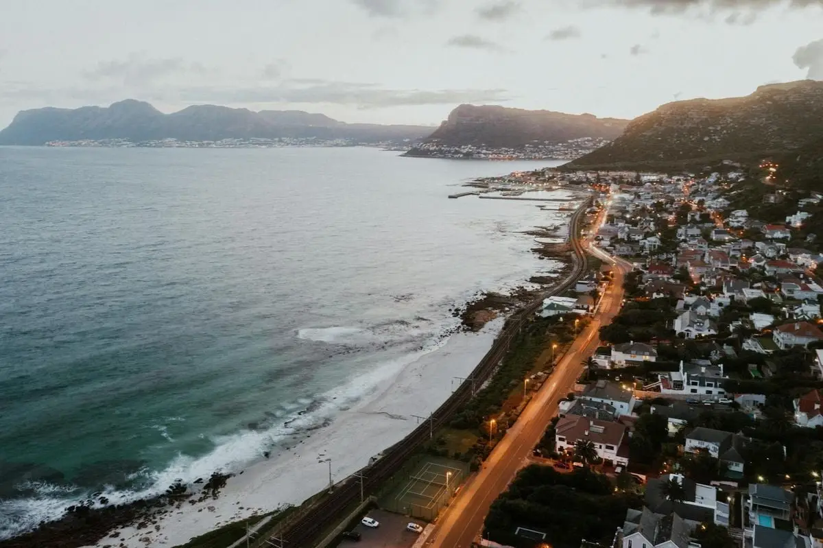 Drone view of a picturesque coastal city at twilight with mountains and illuminated streets.