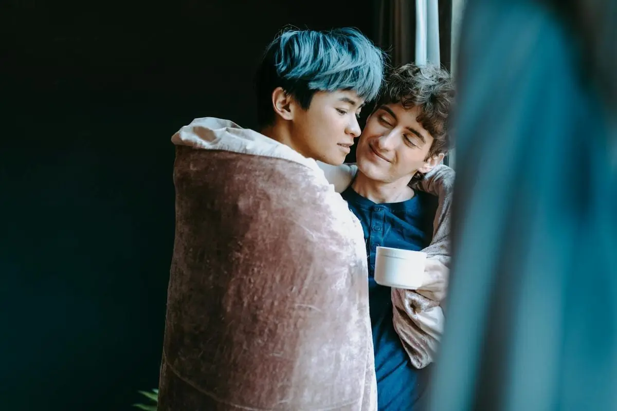An intimate moment with a couple sharing a blanket, enjoying a warm drink indoors.
