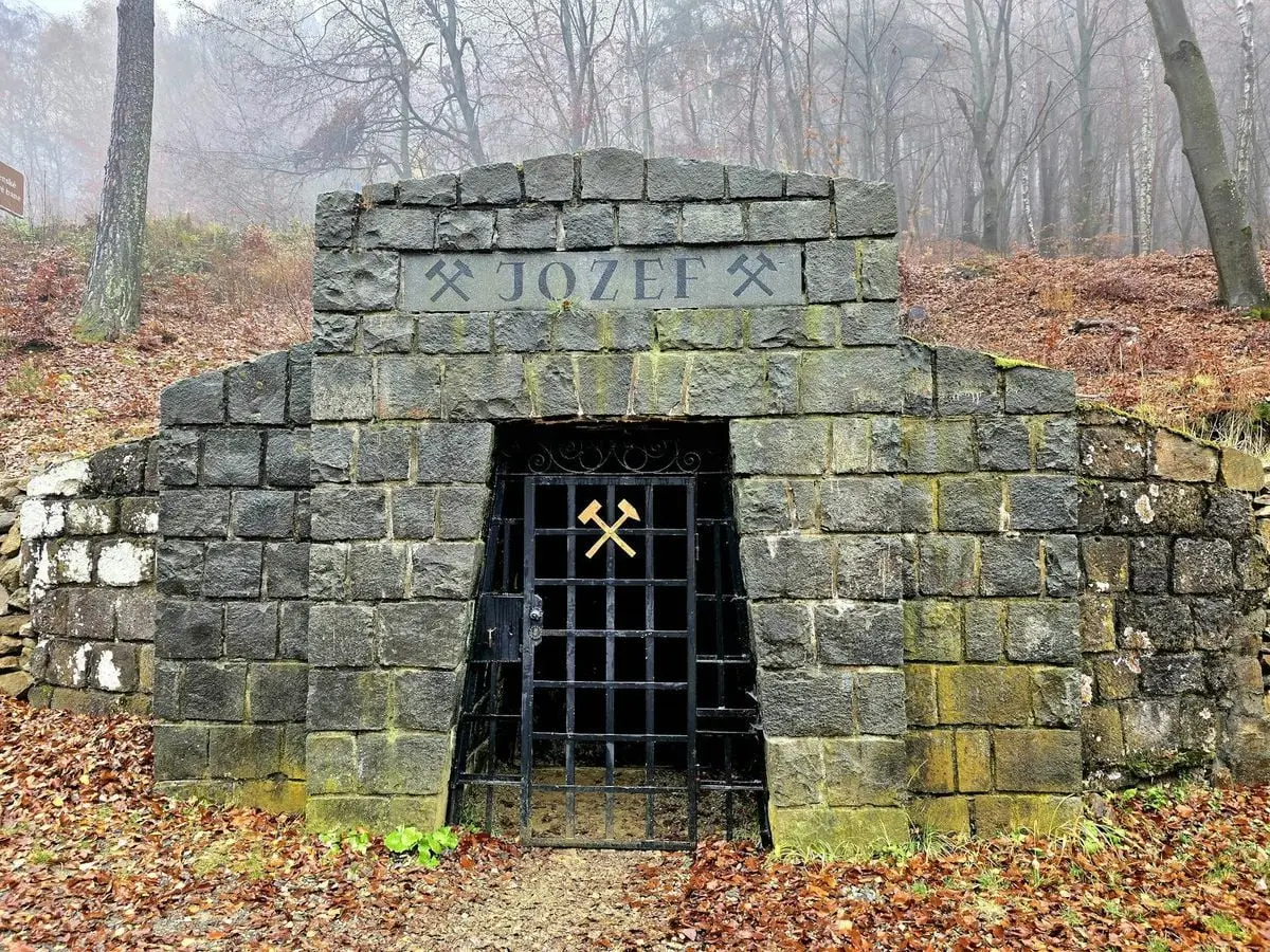 Stone entrance to Jozef mine in autumn forest, highlighting mining heritage.