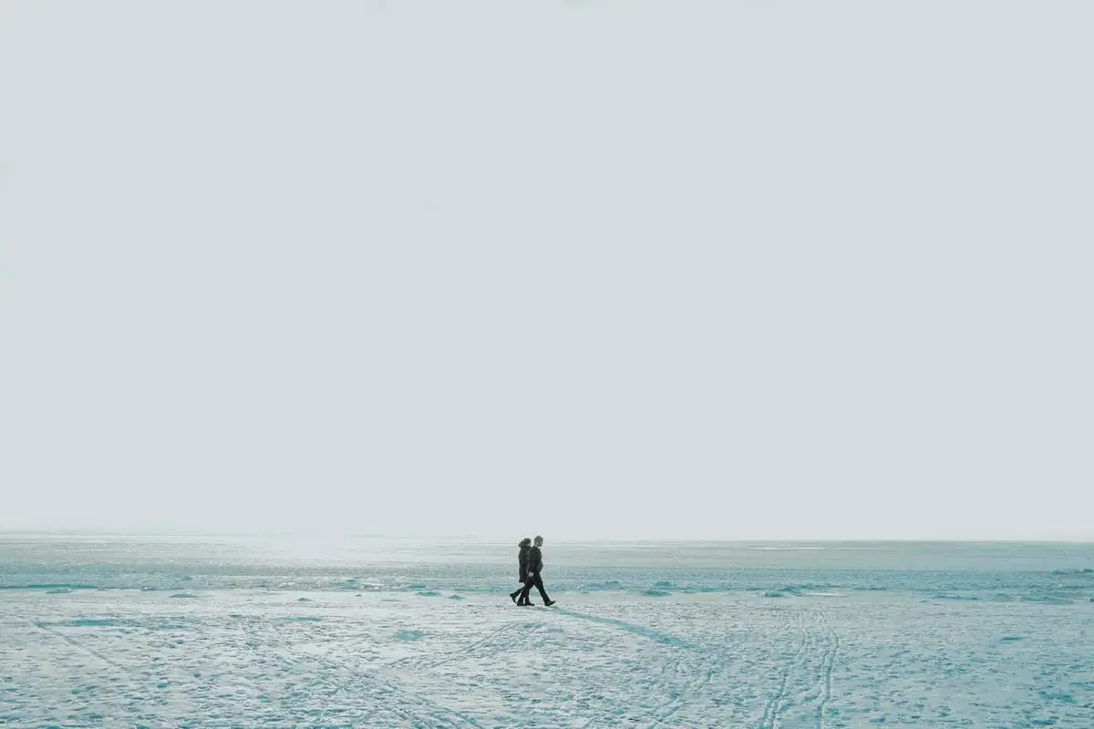 Two individuals walking on a vast snowy landscape under a clear sky, exemplifying solitude and winter serenity.