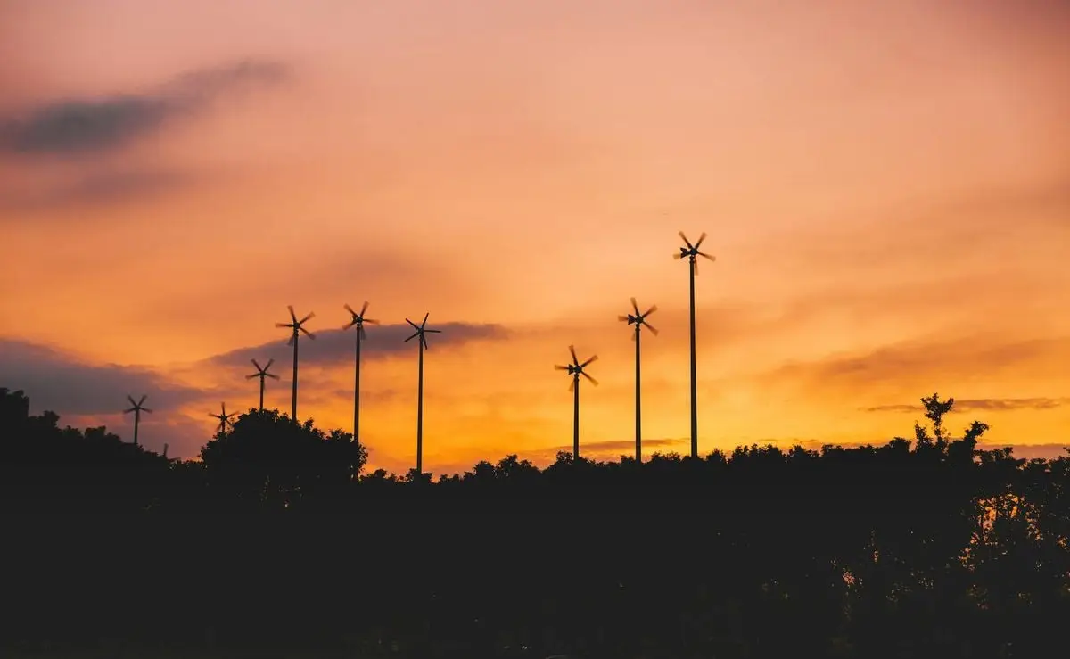 Silhouette of wind turbines against a vivid sunset sky, showcasing renewable energy in nature.