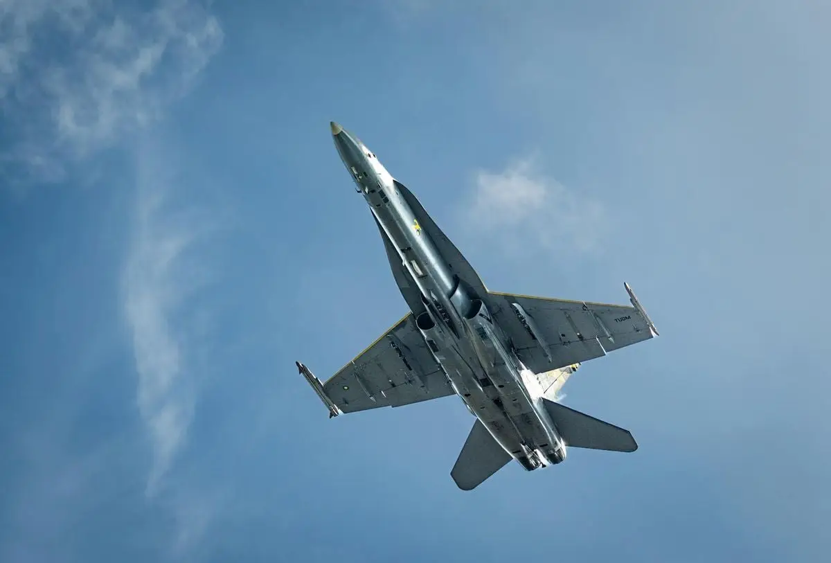 High-angle view of a military jet flying under a clear blue sky, showcasing its structure.