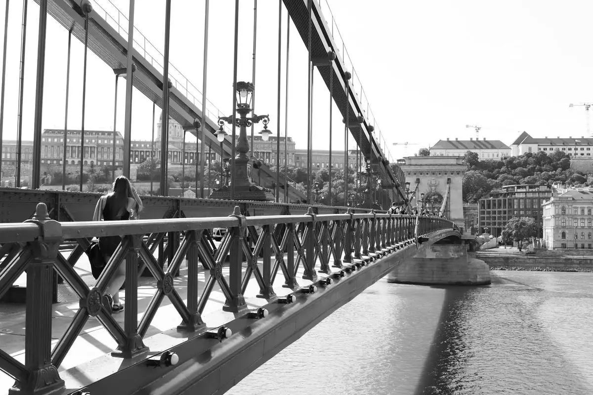 A striking black and white photograph of the Chain Bridge in Budapest, featuring an architectural view across the Danube.