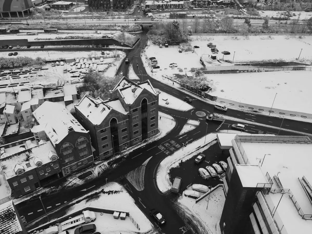 High-angle black and white aerial view of snowy streets and rooftops in Luton, England.