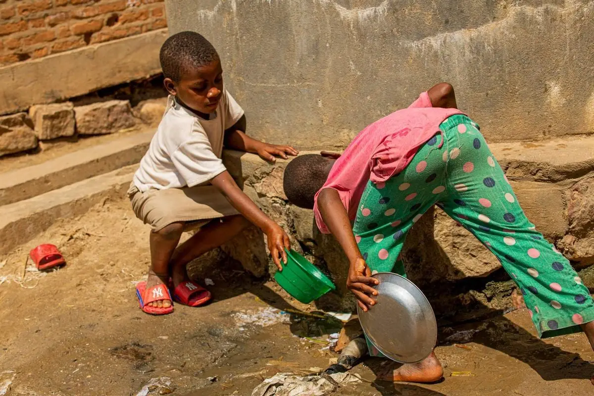 Two children gather water with buckets in an urban setting. Candid street scene.
