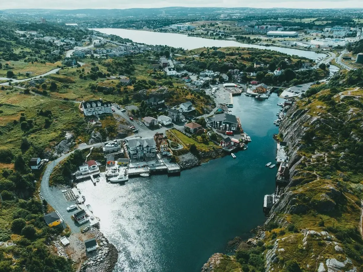 Discover the breathtaking aerial view of a picturesque coastal harbor town surrounded by lush greenery and calm waters.