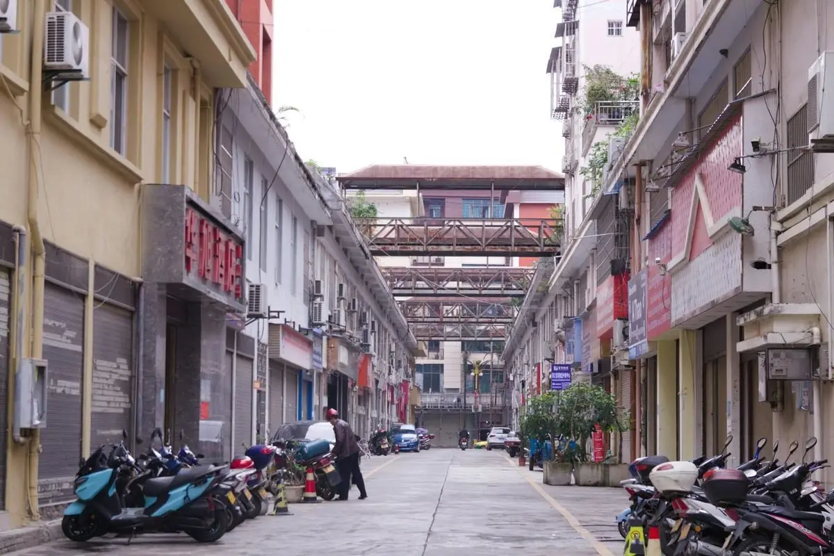 A quiet city street lined with buildings, motorcycles, and a bridge overhead.