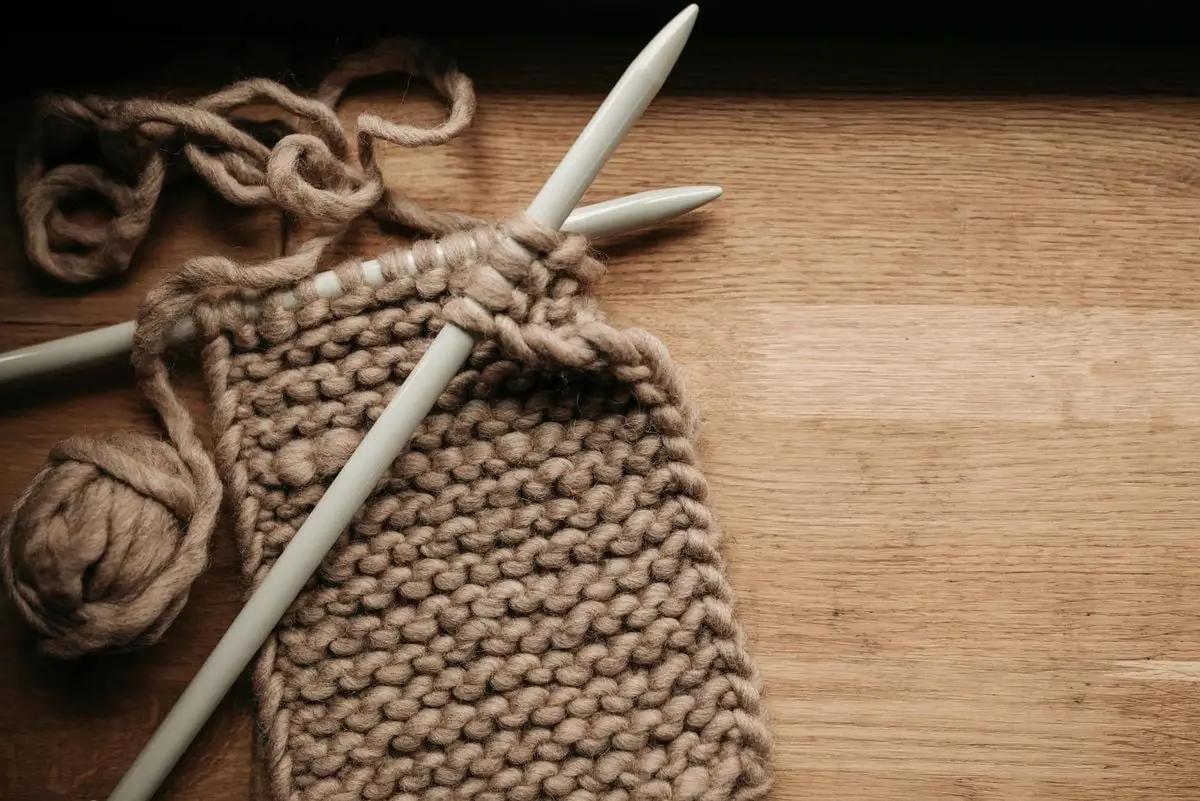 Detailed image of knitting needles, yarn, and a knitting project on a wooden table.