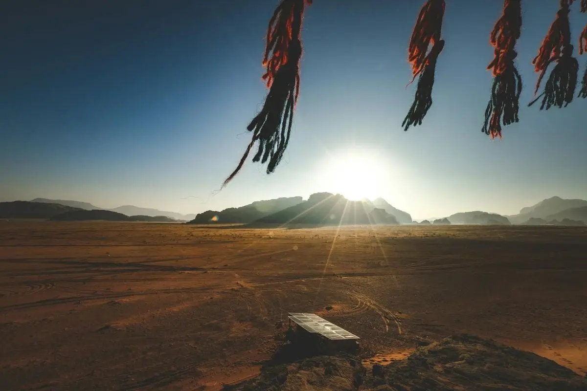 A stunning sunrise over solar panels in a vast desert landscape with mountains in the background.