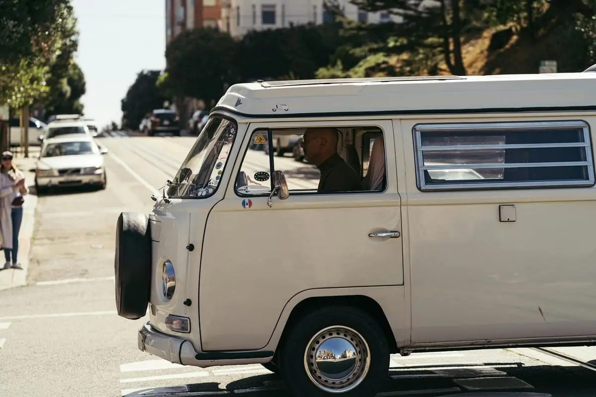 A classic Volkswagen van driving on an urban street in daylight, capturing a nostalgic travel vibe.