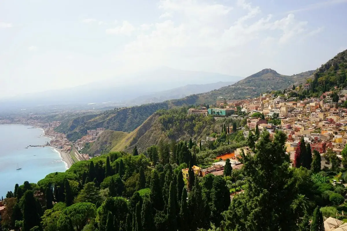A breathtaking view of Taormina, Sicily with lush greenery, coastline, and hills under a summer sky.