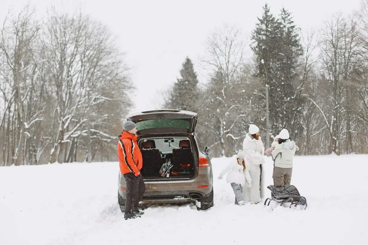 Family in winter gear preparing for outdoor adventure with SUV in snow-covered landscape.