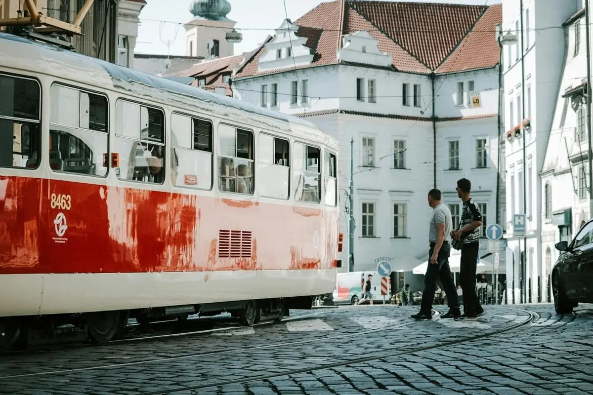 Red and white tram on cobblestone street with people in a European city scene, conveying urban transit vibes.