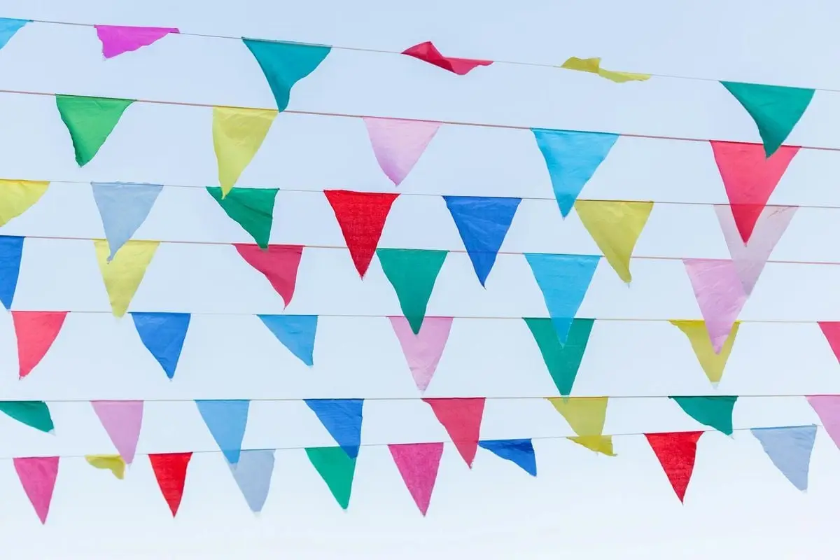 Vibrant and colorful triangular streamers hanging against a clear blue sky, celebrating festival vibes.