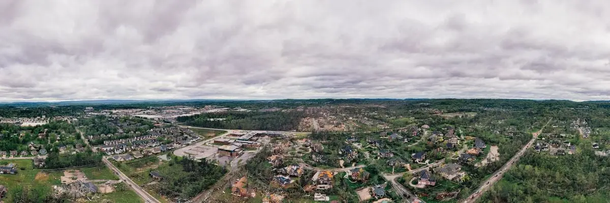 Drone view of peaceful small settlement surrounded with lush greenery against scenic cloudy sky