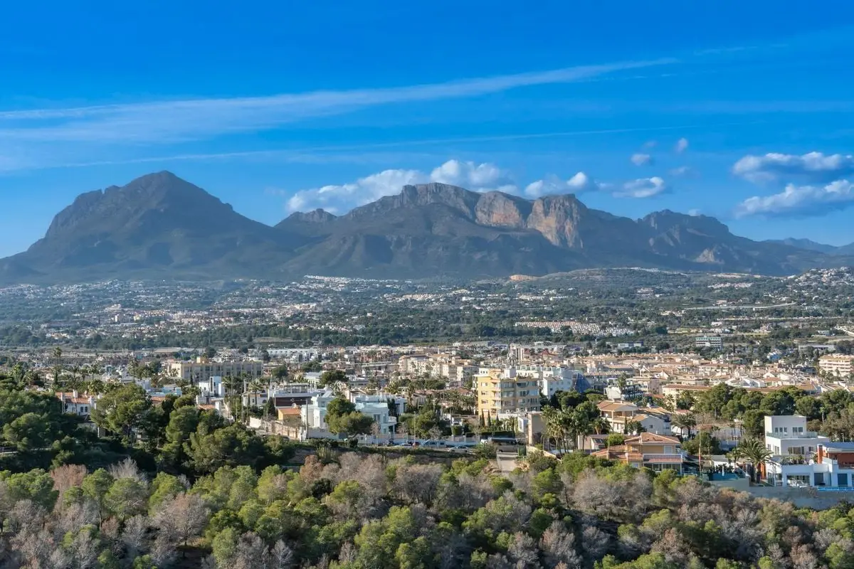 Aerial view of Calpe, Spain, showcasing urban skyline and mountain landscape under a bright blue sky.
