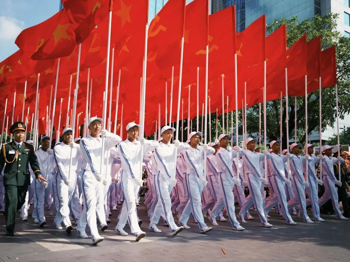 Military personnel marching in uniform under red flags during a daytime parade.