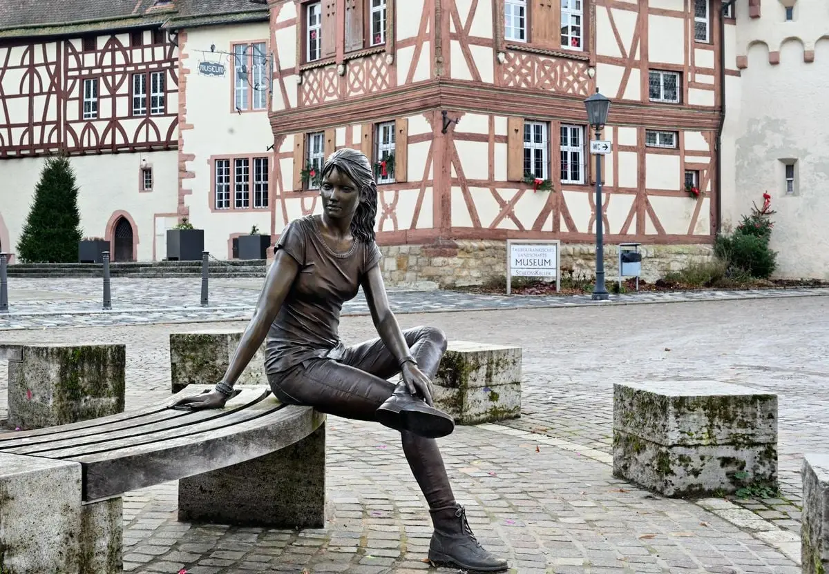 Bronze sculpture on a bench amidst scenic half-timbered houses in Tauberbischofsheim.
