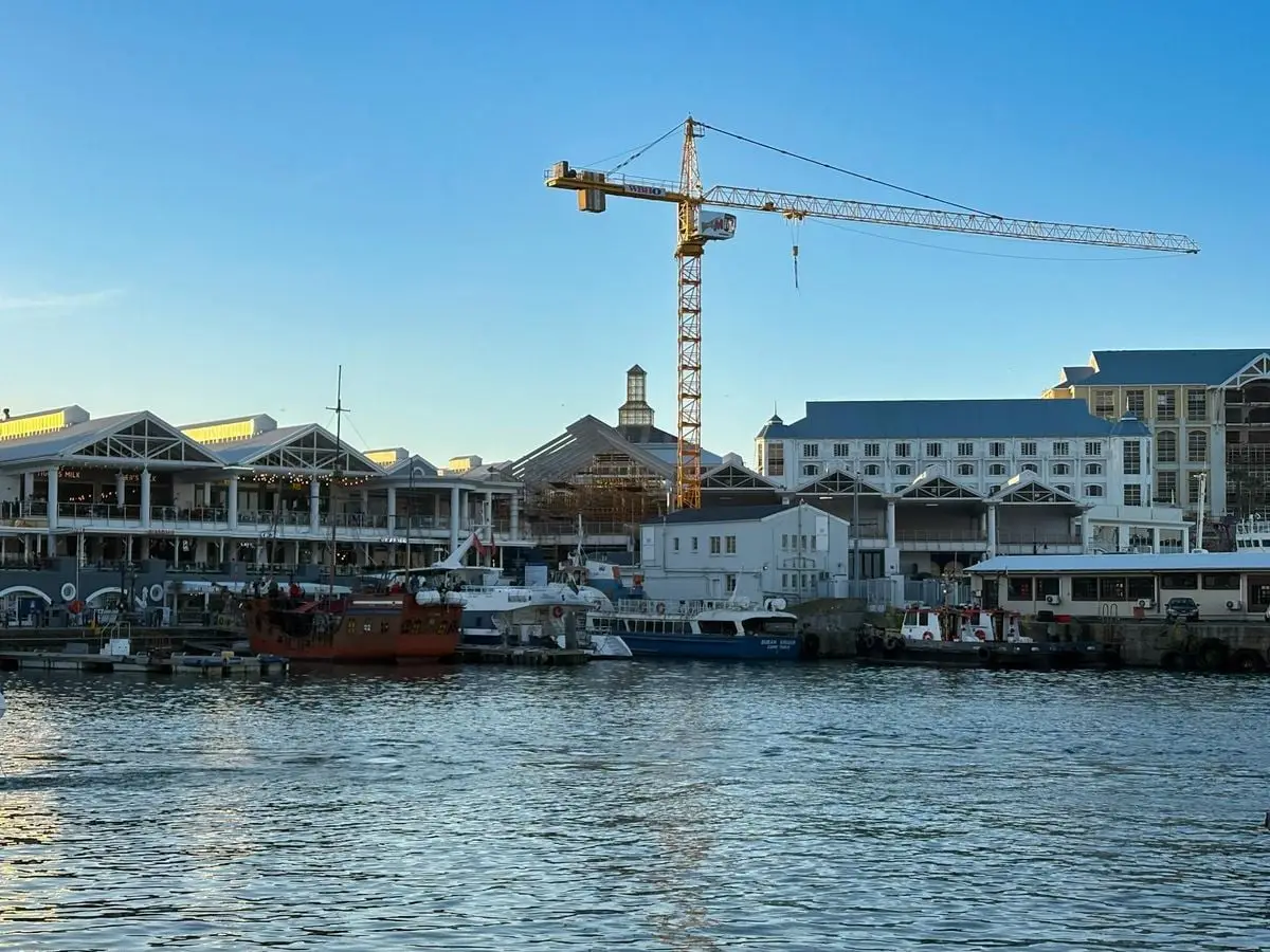 Scenic view of the bustling Cape Town waterfront with a marina and construction crane at sunset.