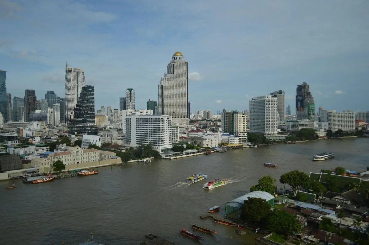 A scenic view of Bangkok's skyline along the Chao Phraya River with boats navigating the water.