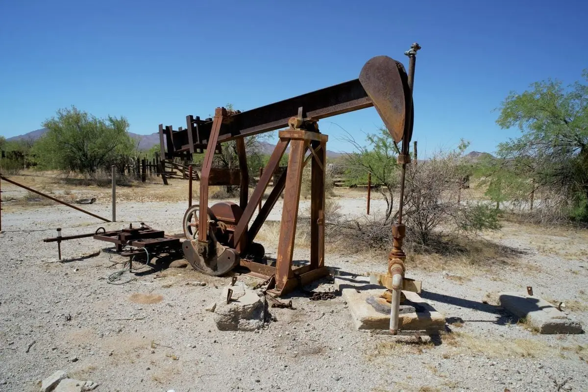 Abandoned rusty oil pumpjack in a barren desert landscape under clear blue skies.