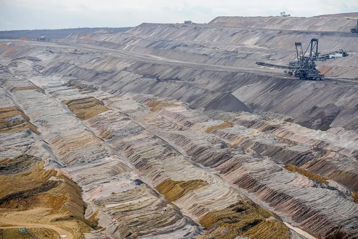 Aerial view of a large, barren open-pit mine featuring machinery and textured soil layers.
