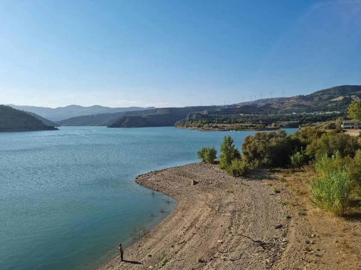 Serene view of a lake in Andalusia with a fisherman on the shore under a clear sky.