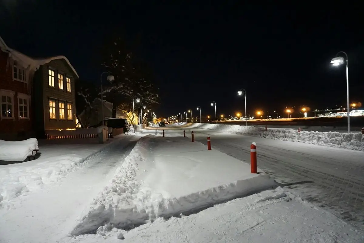 A peaceful, snowy street scene in Akureyri, Iceland, illuminated by streetlights at night.
