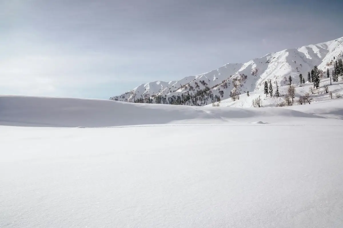 Winter landscape of snow-covered mountains in Gulmarg, Kashmir under clear skies.