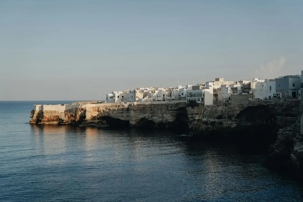 A stunning coastal view of Polignano a Mare in Italy, featuring white cliffside buildings reflecting in the calm sea.