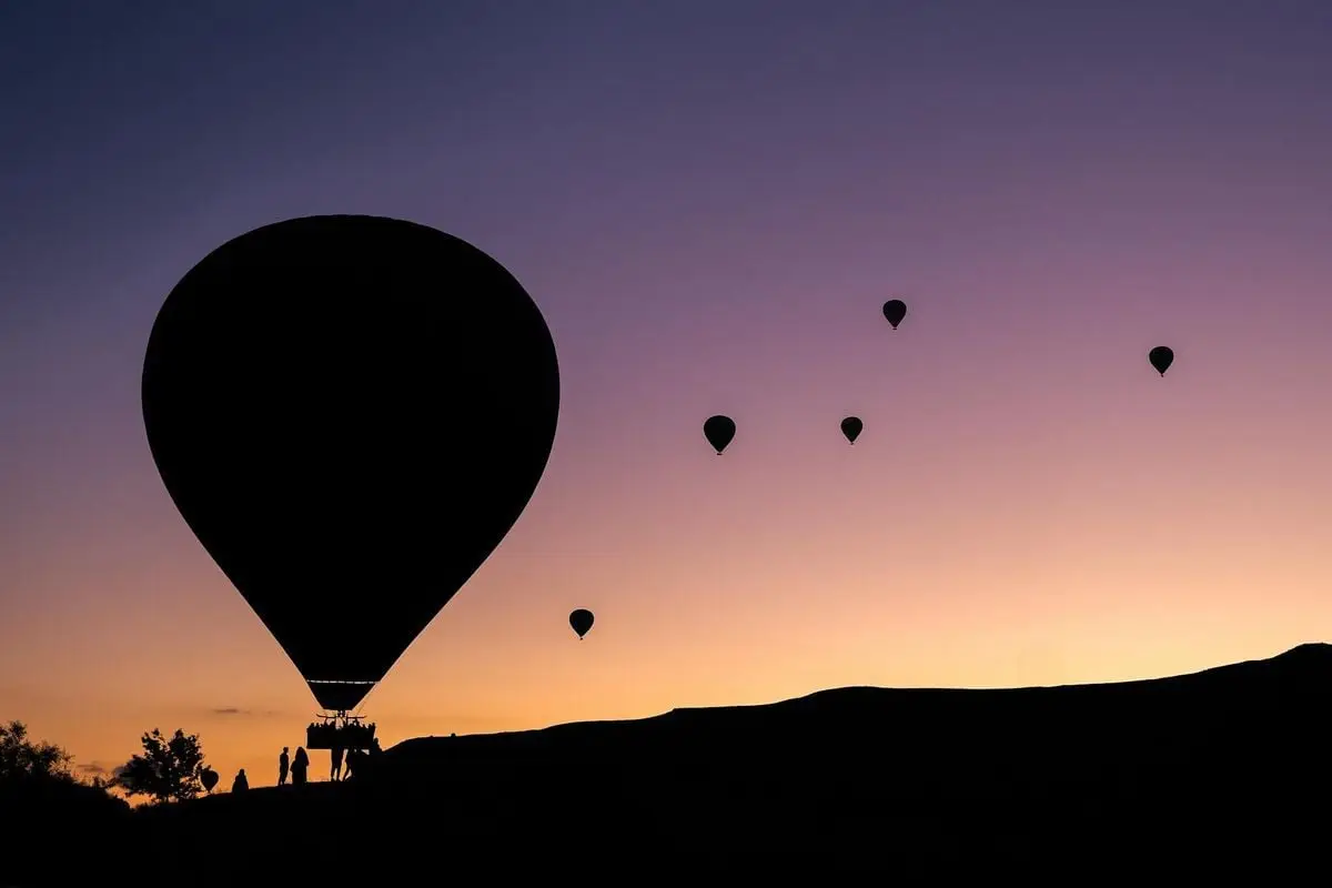 Silhouettes of hot air balloons against a vibrant sunrise sky in Cappadocia, Türkiye.