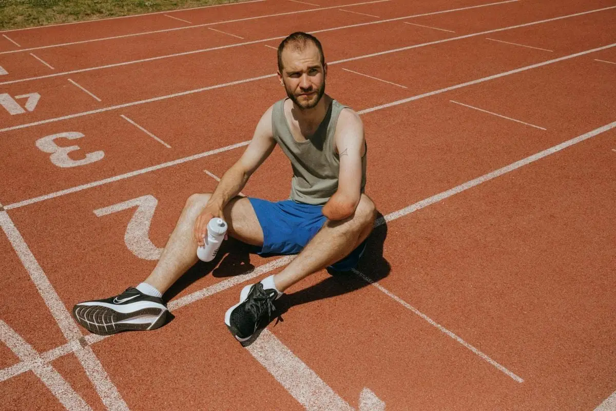 Athlete taking a break on a running track with a water bottle in sunlight.