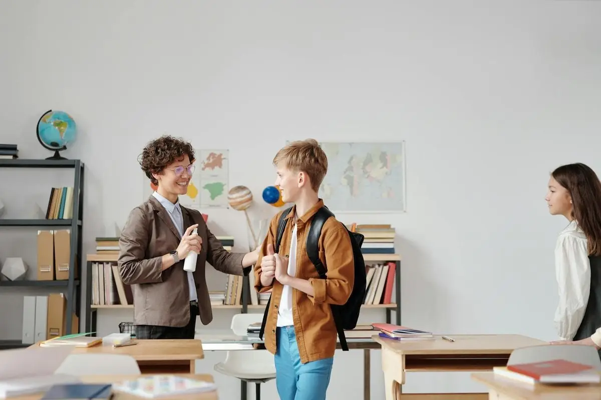 Teacher uses hand sanitizer while interacting with students in a classroom setting.