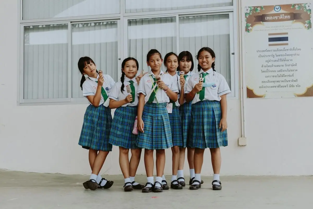 Six schoolgirls in uniform enjoying ice cream outside their school building in Thailand.