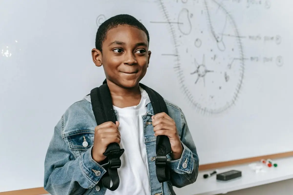 A cheerful African American boy with a backpack in a classroom setting.