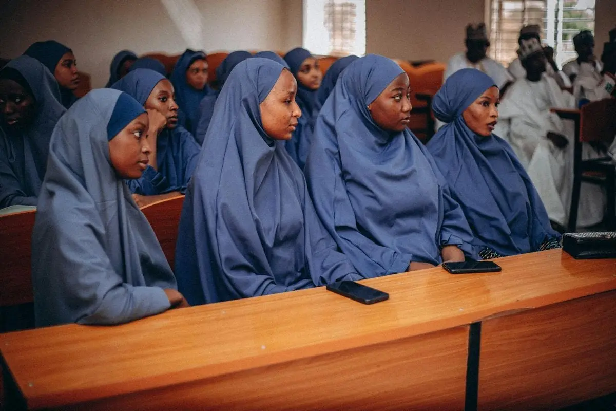 A group of young women in blue hijabs attentively attending a classroom lecture.