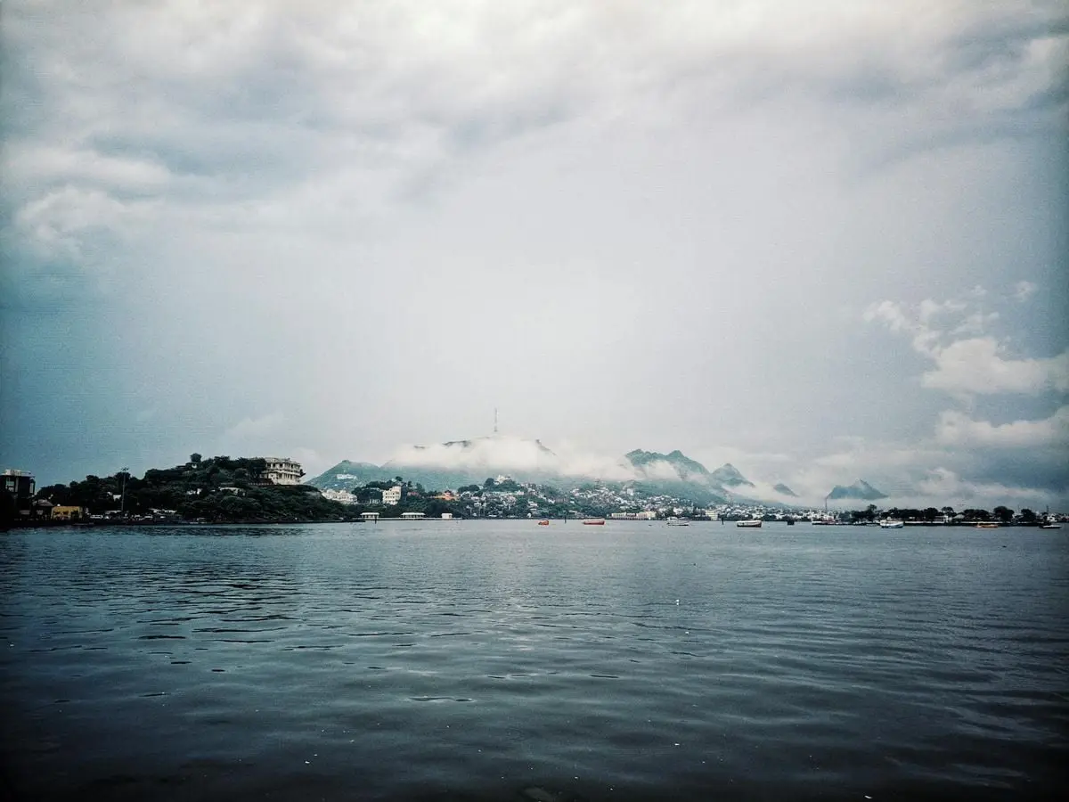 Beautiful landscape of a lake with a town and mountains in the distance under a cloudy sky.