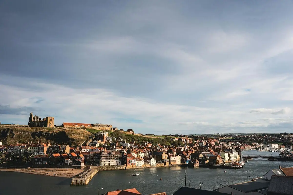 A picturesque coastal town with historic ruins and river under a vast sky.