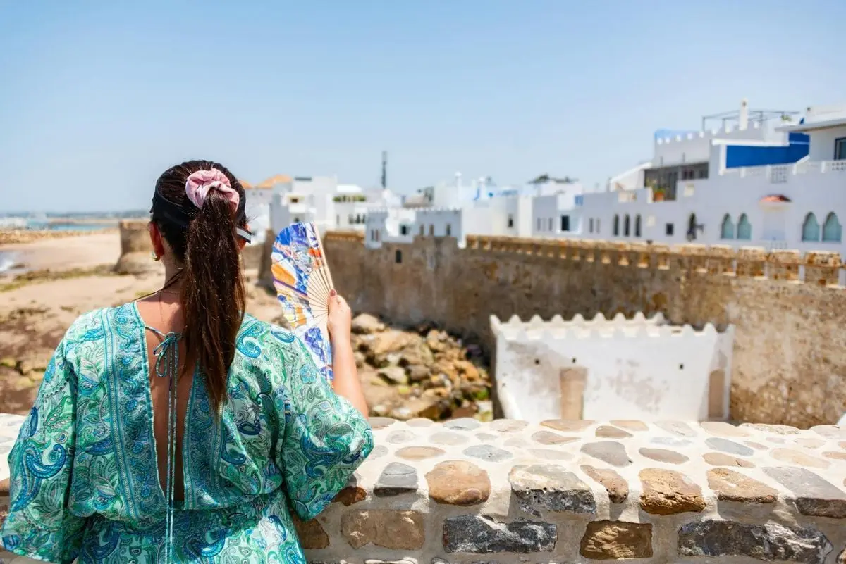 A woman admires the scenic view of a historic Moroccan seaside town. Perfect for travel and photography sites.